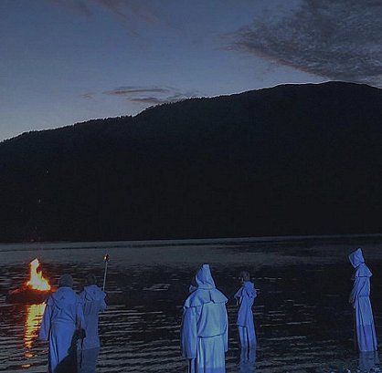 Hooded figures by water's edge, boat burning in water