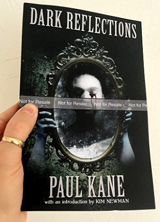 photograph of a man's hand holding a copy of Dark Reflections, by Paul Kane, to show the front cover