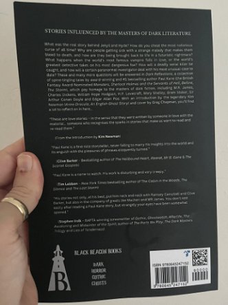 photograph of a man's hand holding up a copy of Dark Reflections by Paul Kane, showing the back cover of the book