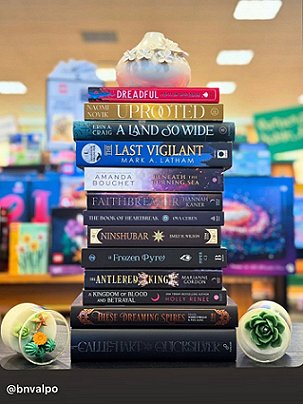 photograph of a pile of hardback books standing on a dark shelf in a bookstore. Second from the bottom is a copy of These Dreaming Spires, edited by Marie O'Regan and Paul Kane