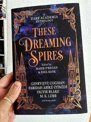 photograph of a man's hand holding a copy of These Dreaming Spires, edited by Marie O'Regan and Paul Kane, up against a white background