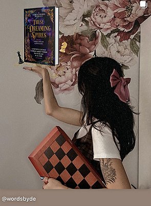 photograph of author De Elizabeth standing turned away from the camera. In her upheld hand is a copy of These Dreaming Spires, edited by Marie O'Regan and Paul Kane, with a black and a white chess piece on each side. In her left hand, De is holding a pink and black chessboard