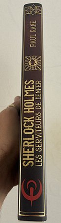 photograph of a hand holding up a copy of the French edition of Sherlock Holmes and the Servants of Hell by Paul Kane, showing the spine of the book