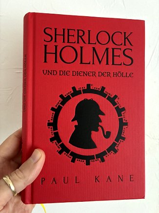 photograph showing a man's hand holding up the German edition of Sherlock Homes and the Servants of Hell by Paul Kane, showing the hardcover inside the dustjacket