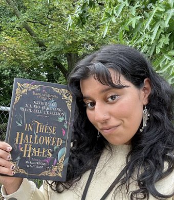photograph of a young woman with long dark hair holding up a copy of In These Hallowed Halls, edited by Marie O'Regan and Paul Kane, in front of a wooded background