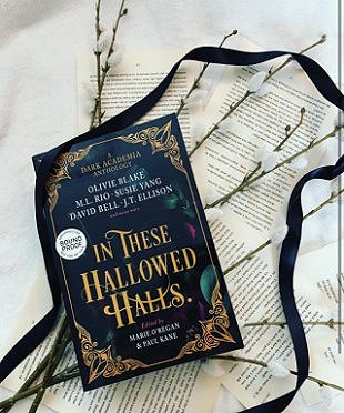 A copy of In These Hallowed Halls lying on a background of typed pages, with willow branches and a black ribbon
