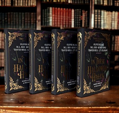 A display of four standing copies of In These Hallowed Halls, on a wooden surface in front of full bookshelves