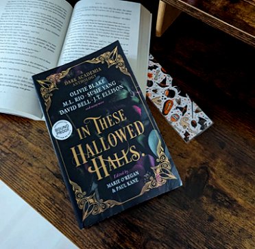 Picture showing a copy of In These Hallowed Halls, edited by Marie O'Regan and Paul Kane, lying on an open book with a bookmark alongside, on a wooden surface