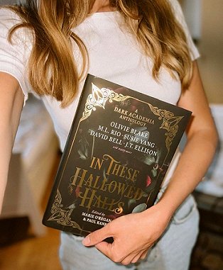 photograph of a woman with long hair holding a copy of In These Hallowed Halls, edited by Marie O'Regan and Paul Kane
