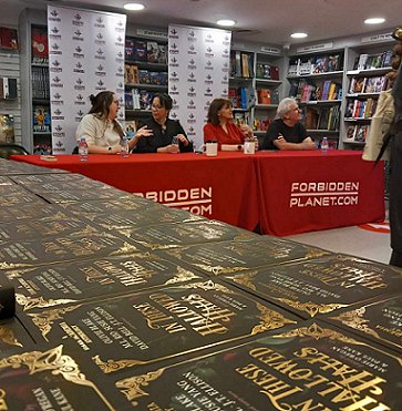 Photo showing a display of copies of In These Hallowed Halls in the foreground, with the authors in the background seated at a red-clothed table. L to R: Tori Bovalino Helen Grant, Marie O'Regan and Paul Kane