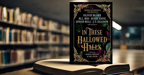 photgraph of a copy of In These Hallowed Halls, edited by Marie O'Regan and Paul Kane, standing on top of an open hardback book on a wooden surface. The wall behind the book is lined with bookshelves