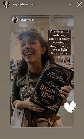 screenshot from @kayaydrew showing a smiling young woman in a dark green top holding up a copy of In These Hallowed Halls, edited by Marie O'Regan and Paul Kane. text reads This delightful anthology came out today featuring a story from my love and light @kayaydrew