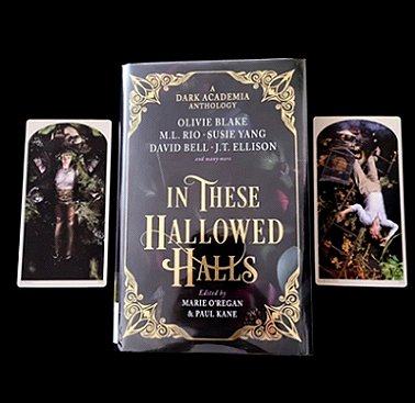 photograph of a copy of In These Hallowed Halls, edited by Marie O'Regan and Paul Kane, lying on a black surface. A card lies to either side, teh one on the left featuring a prone female figure, the one on the right featuring a prone male figure