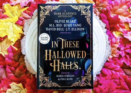 A copy of In These Hallowed Halls, edited by Marie O'Regan and Paul Kane, lying on a white circle, surrounded by pink red and yellow autumnal leaves