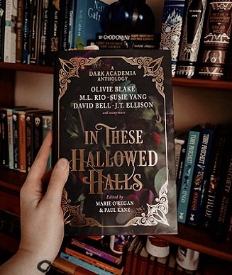 image of a hand holding a copy of In These Hallowed Halls, edited by Marie O'Regan and Paul Kane, up against rows of bookshelves