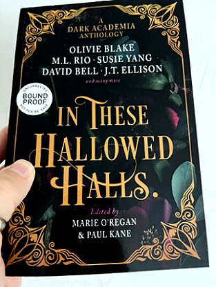 A man's hand holding an advanced review copy of In These Hallowed Halls, edited by Marie O'Regan and Paul Kane