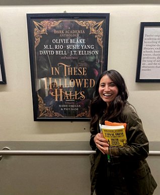 Image of Olivie Blake standing next to a poster of the cover of In These Hallowed Halls, edited by Marie O'Regan and Paul Kane