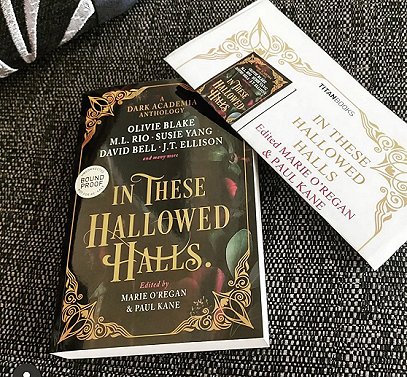 Photograph of a copy of In These Hallowed Halls, edited by Marie O'Regan and Paul Kane, against a dark cloth background and beside a copy of the press release for In These Hallowed Halls