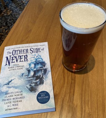 copy of a book, The Other Side of Never, edited by Marie O'Regan and Paul Kane, on a table next to a pint of beer