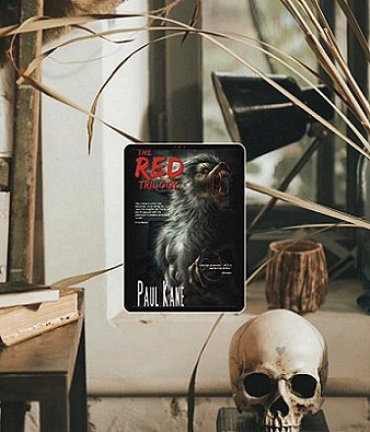 image showing a tablet featuring the cover of The RED Trilogy by Paul Kane on a cream windowledge, beside a wooden pot. In the foreground is a skull, and a book on a wooden table. In the background are a plant and a black lamp.