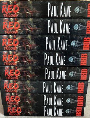 photograph showing the spines of a stack of six copies of The RED Trilogy by Paul Kane