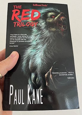 photograph showing a man's hand holding up a copy of The RED trilogy by Paul Kane