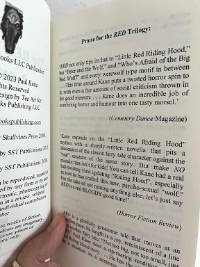 photograph of a man's hand holding a copy of The RED trilogy by Paul Kane open at the Praise for the RED trilogy page