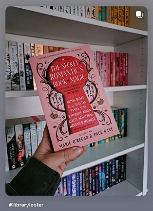 photograph of a hand holding a copy of The Secret Romantic's Book of Magic, edited by Marie O'Regan and Paul Kane, up against filled white bookshelves