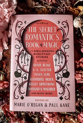 photograph of a copy of The Secret Romantic's Book of Magic, edited by Marie O'Regan and Paul Kane, on a bed of pink flowers