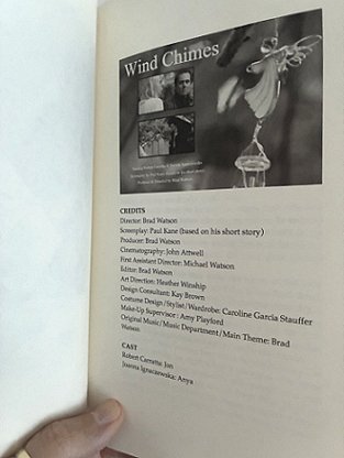 photograph showing a man's hand holding a copy of Short Sharp Shocks by Paul Kane, open to the title page for Wind Chimes