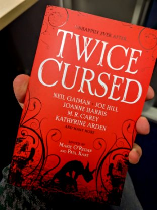 Image showing a hand holding a copy of the book Twice Cursed, edited by Marie O'Regan and Paul Kane