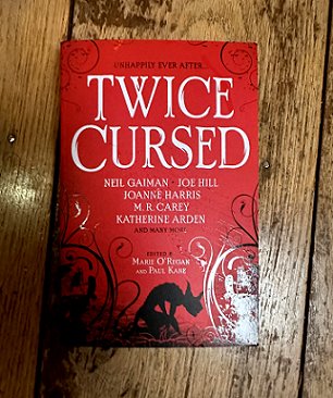 Book on a wooden surface. Twice Cursed, edited by Marie O'Regan and Paul Kane