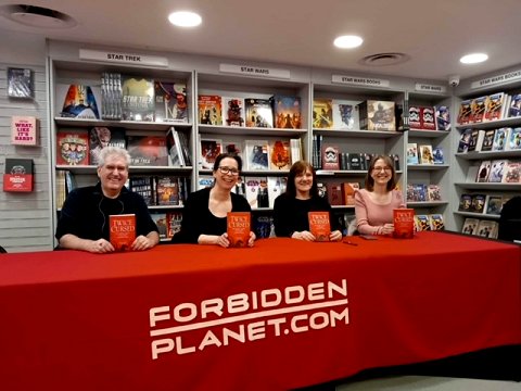 Twice Cursed editors and authors sitting at a table with a Forbidden Planet cloth, holding copies of Twice Cursed. L to R: Paul Kane, Helen Grant, Marie O'Regan and Laura Purcell