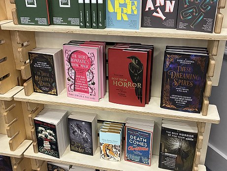 photograph showing display shelves at the Waterstones Dealers table at WFC 2025. Features In These Hallowed Halls, These Dreaming Spires, The Secret Romantic's book of Magic and Death Comes at Christmas, all edited by Marie O'Regan and Paul Kane