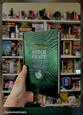 photograph of a hand holding a copy of Beyond and Within Witchcraft, edited by Marie O'Regan and Paul Kane, up against bookshelves in the background