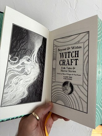 photograph showing a man's hand holding up a copy of Beyond & Within: Witchcraft, edited by Marie O'Regan and Paul Kane, to show the title page and the illustration of an upside down woman's head, with long hair flowing downwards
