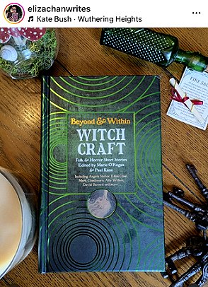 screenshot from @elizachanwrites. Photograph of a copy of Beyond and Within Witchcraft, edited by Marie O'Regan and Paul Kane, on a wooden surface. Around the book are: a bunch of iron keys, a jar containing moss and toadstools, a hairbrush and a piece of card with a pen wrapped in red ribbon beside it