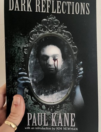 photoraph of a man's hand holding up a copy of Dark Reflections by Paul Kane