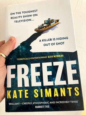 Man's hand holding a copy of Freeze by Kate Simants