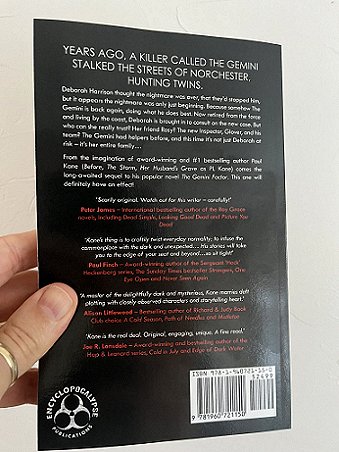 image of a man's hand holding up a copy of a book, The Gemini Effect by Paul Kane, to show the back cover