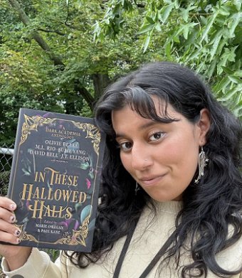 photograph of a young woman with long dark hair holding up a copy of In These Hallowed Halls, edited by Marie O'Regan and Paul Kane, in front of a wooded background