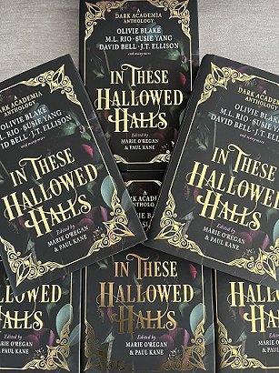 A display of six copies of In These Hallowed Halls, edited by Marie O'Regan and Paul Kane, lying on a grey background