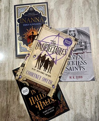 A display of four books on a marbled surface, including a copy of In These Hallowed Halls, edited by Marie O'Regan and Paul Kane