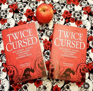Book display featuring an apple and two copies of Twice Cursed, edited by Marie O'Regan and Paul Kane on a cloth with black and white skulls and red roses