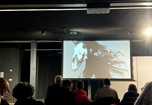 TV screen with painted image of horse's head, in front of an audience